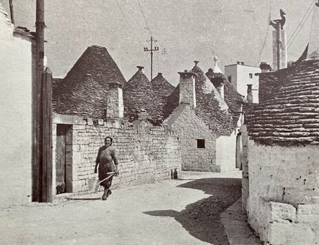 Un vicolo tra i trulli con una donna che lo attraversa, fotografia d'epoca